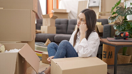Young beautiful hispanic woman sitting on floor with upset expression at new home