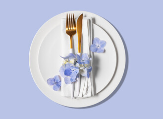 Festive table setting with blue hydrangea flowers and white plates on a blue background. The concept of celebrating women's day, birthday or mother's day.