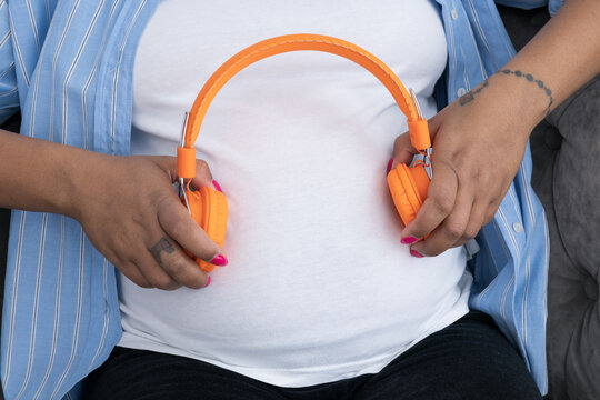 A pregnant woman puts headphones to her stomach