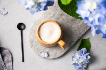 Spring bouquet with blue hydrangea flowers and a cup of cappuccino coffee in a yellow cup and spoon on a light background. The concept of a morning drink for breakfast.