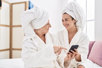 Obraz na płótnie Canvas Mother and daughter wearing bathrobe using smartphone at bedroom