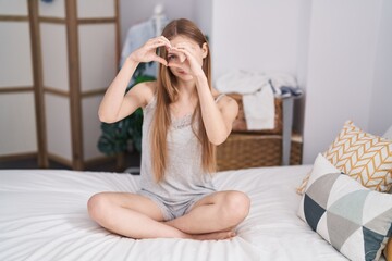 Young caucasian woman doing heart gesture sitting on bed at bedroom