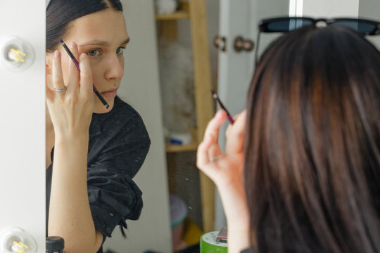 a young girl applies makeup herself at home in front of a mirror