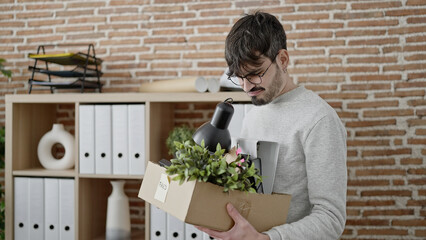 Young hispanic man being fired packing belongings from workplace at office