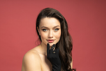 Portrait of a brunette in mittens with jewelry, on a pink background