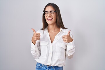 Young brunette woman wearing glasses success sign doing positive gesture with hand, thumbs up smiling and happy. cheerful expression and winner gesture.