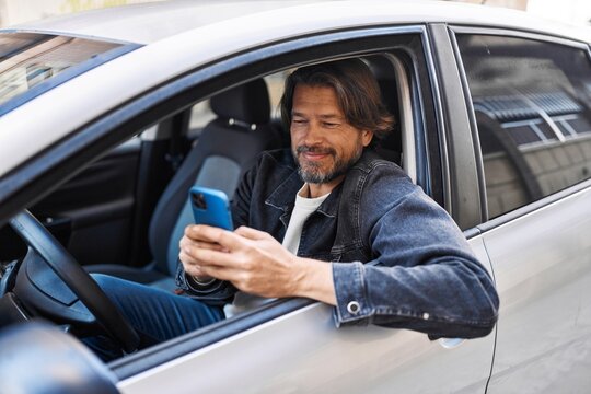 Middle age man using smartphone sitting on car at street