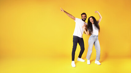 Middle eastern couple pointing finger at copy space, yellow background