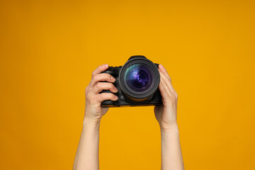 Close-up of a camera in hands on a yellow background