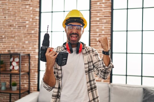 Young hispanic man with beard working at home renovation screaming proud, celebrating victory and success very excited with raised arms