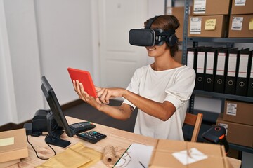 Young beautiful hispanic woman ecommerce business worker using virtual reality glasses and touchpad at office