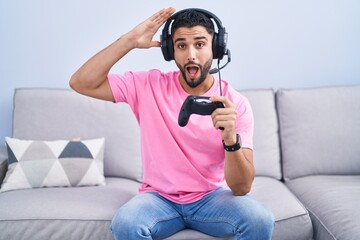 Hispanic young man playing video game holding controller sitting on the sofa crazy and scared with hands on head, afraid and surprised of shock with open mouth © Krakenimages.com