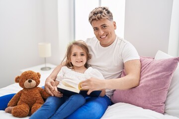 Father and daughter father and daughter reading book holding teddy bear at bedroom