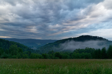 Wieczór w dzikich Bieszczadach, opadające mgły nad zielonymi górami.