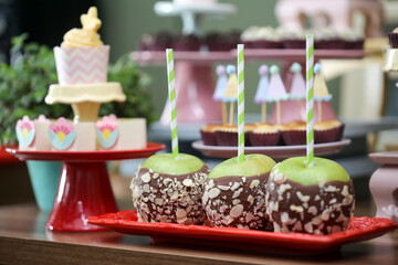 Maçãs do amor irresistíveis em uma versão especial, com maçãs verdes cobertas até a metade com chocolate e crocante de pistache, fazendo sucesso em uma animada festa infantil.