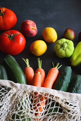 Mesh bag with fresh seasonal fruit and vegetable. Selective focus, dark background.