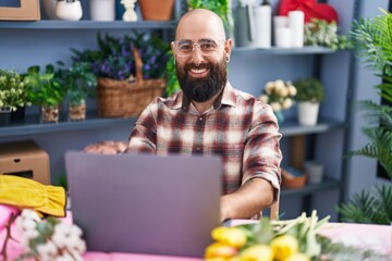 Young bald man florist smiling confident using laptop at flower shop