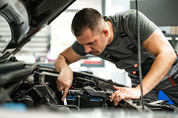 Fototapeta na wymiar young mechanic in workshop repairs car engine with key