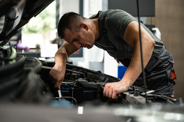 Fototapeta na wymiar young mechanic in workshop repairs car engine with key