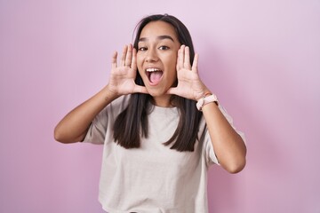 Young hispanic woman standing over pink background smiling cheerful playing peek a boo with hands...