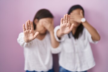 Hispanic mother and daughter together covering eyes with hands and doing stop gesture with sad and fear expression. embarrassed and negative concept.