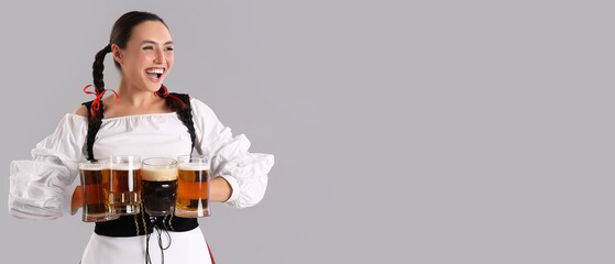 Young Oktoberfest waitress with mugs of beer on grey background with space fro text