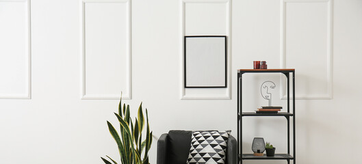 Black armchair with houseplant and shelving unit near white wall with hanging blank frame. Banner for design