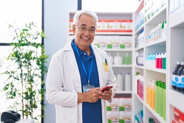 Middle age grey-haired man pharmacist using smartphone working at pharmacy