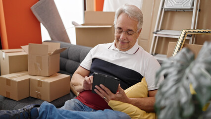 Middle age man with grey hair sitting on the sofa using tablet at new home