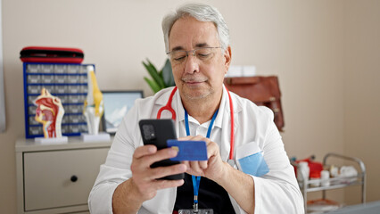 Middle age man with grey hair doctor using smartphone working doing online shopping at clinic