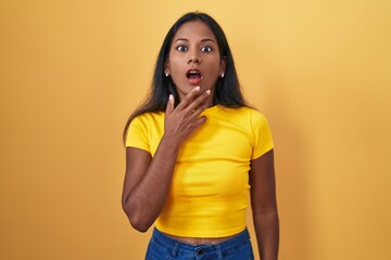 Young indian woman standing over yellow background looking fascinated with disbelief, surprise and...