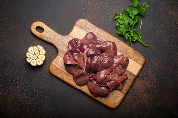 Raw chicken liver on wooden cutting board top view on dark rustic concrete background kitchen table with parsley and garlic. Healthy food ingredient, source of iron, folate, vitamins and minerals - 622042749
