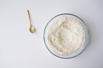 Preparing the dough, white flour in a bowl on a white background with a spoon of ingredients, ready...