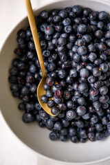 Close-up of a white bowl of dried wild blueberries with a golden spoon, top view