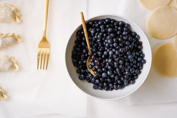 Blubbery in white bowl with golden spoon, fresh berries ready for ad in dough for making varenyki. Top view of homemade traditional cooking
