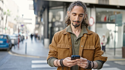 Fototapeta premium Young hispanic man using smartphone with serious expression at street
