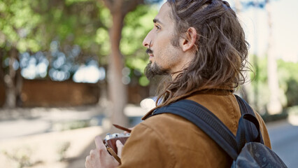 Young hispanic man tourist wearing backpack make photo at park