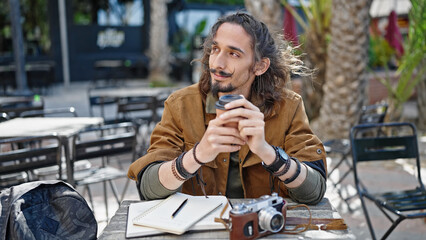Young hispanic man tourist drinking coffee sitting on table at coffee shop terrace