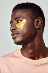 Portrait of a young African American man with hydrogel patches under his eyes in the studio. Young...
