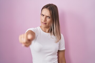 Blonde caucasian woman standing over pink background pointing displeased and frustrated to the camera, angry and furious with you