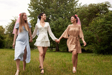 A happy charming bride in a white dress with a white veil and two bridesmaids in a blue and beige...