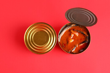Tin cans with fish in tomato sauce on red background