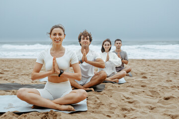 Women and men sitting in lotus pose, holding hands in namaste, enjoying spiritual meditation on the beach, free space