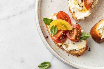 Bruschetta sandwiches with tomatoes, cream cheese, olive oil and basil on a plate on white marble background, top view, copy space. Traditional italian antipasti