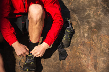 A man in a red jacket ties his hiking shoes, closeup