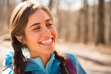 A young woman in a blue jacket smiles while hiking in the outdoors, closeup
