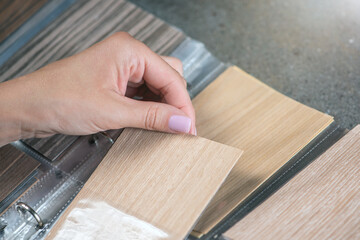Fototapeta na wymiar Samples of chipboard. A close-up woman's hand takes out a chipboard sample from a wood swatch palette. Design or renovation of premises, furniture production.