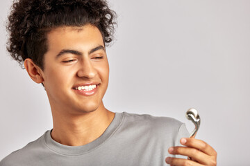 Young handsome smiling guy using de-puffing face roller to keep his skin soft and smooth. Swarthy man with black curly hair maintaining his natural beauty with skincare routine. Men's self-care.