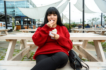 young latin woman outdoors looking at the camera and taking a portion of ice cream to her mouth