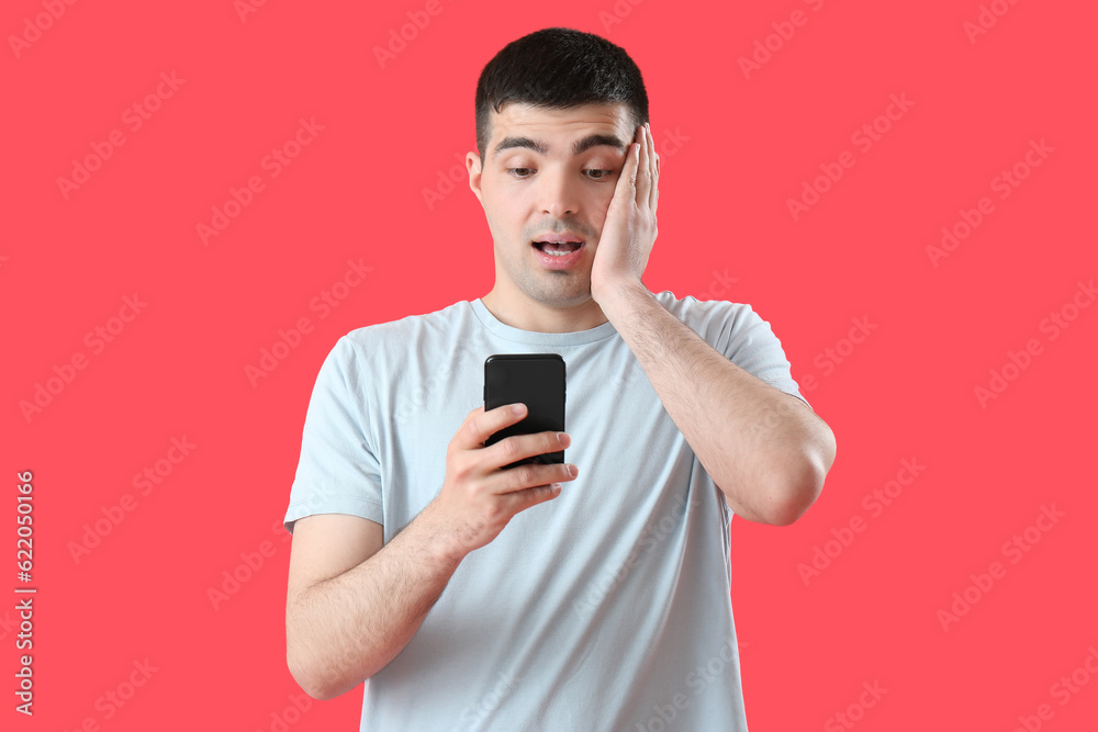 Poster Surprised young man with smartphone on red background